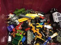 Photo showing a large bin filled with a variety of vintage diecast cars and trucks including construction vehicles and military tanks.