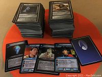 Image showing two large stacks of Star Trek gaming cards with some cards laid flat in front featuring characters and game information, one card back with Starfleet emblem visible