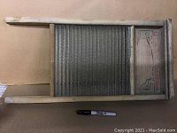 Full view of antique washboard showing wooden frame and glass scrubbing surface with pen for size reference