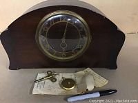 Antique Seth Thomas wooden mantel clock shown with winding key, pendulum bob and paperwork below it.