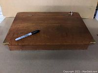 Full view of closed antique wooden writing slope desk with black marker on top for size reference