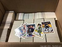 Open box showing tightly packed stacks of hockey cards with some cards laid on top showing various players in retro uniforms and different card designs.