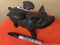 Close-up side view of cast iron pig doorstop next to Sharpie marker for size scale.