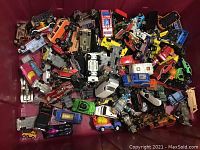 Top view showing a large collection of vintage diecast cars and trucks in mixed colors and conditions piled in a storage bin.