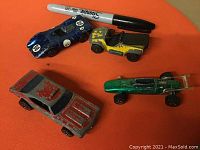 Top view of four vintage Hot Wheels RedLine toy cars with a Sharpie pen for scale.