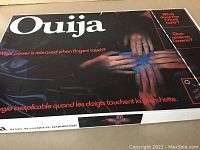 Top view photo of Ouija box showing hands on blue planchette and English/French text