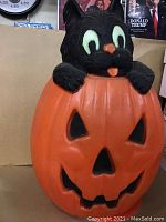 Front view of the vintage hollow jack-o'-lantern pumpkin with black cat on top showing facial features and hollow openings for light.