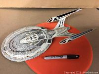 Full top view of the vintage Star Trek starship toy placed on an orange surface with a marker for size reference to show scale and design details.