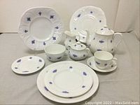 Overview photo showing a variety of dishes including plates, cups, saucers, creamers, sugar bowl, teapot with charger all decorated in blue floral pattern on white bone china.