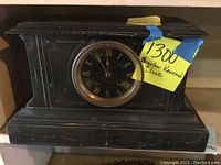 Front view of the black wooden mantel clock with floral carvings and Roman numeral dial with brass bezel.