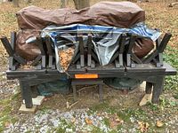 Stack of black painted outdoor picnic table, benches and stools shown upside down outdoors under tarp, some wear and weathering visible