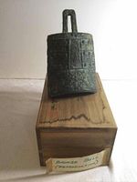 Replica bronze Pien-Chung bell with a rectangular body and loop handle, showing engraved patterns and aged green patina. Placed on original wooden box with inscriptions.