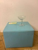 Single champagne glass with wide shallow bowl, slender stem, on top of a light blue Tiffany & Co. box