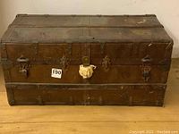 Front view of the worn brown steamer trunk showing metal reinforcements and latches