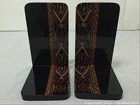 Front view of pair of black lacquer bookends with handpainted traditional geometric and floral patterns in gold and red hues.