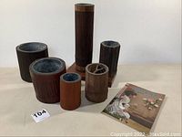 Front view of eight wooden ikebana vases of varying sizes arranged on a table, showing natural wood textures and several dark brown finishes.