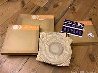 Three flat cardboard boxes labeled “AKARI Lamps by Isamu Noguchi” with one opened showing wrapped paper shade and instruction sheet