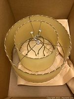 Top view of two stacked yellow fabric lampshades with braided trim showing metal harp and spider fitting centers.