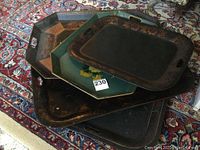 Five large metal platters stacked showing variety of shapes, colors, and hand-painted borders.