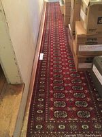 Long view of red oriental runner carpet laid out in a hallway, showing full length and narrow width.