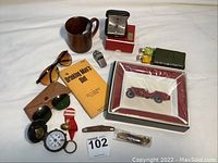 Overview of lot with all items including mug, sunglasses, book, knives, clock, ashtray, keys and other collectibles