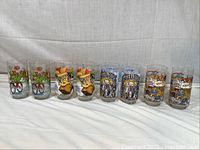 Full set of 8 collectible glasses displayed in a row on a fabric background, featuring colorful Muppet character designs.