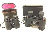 Two binoculars side by side, one with leather carrying case open showing pink lining, the other with hard black case closed.