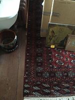 Photo showing corner and edge of red Oriental carpet with boxes and artwork placed on it.