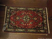 Full view of small rectangular oriental-style throw rug on wooden floor showing red central medallion and multiple borders.