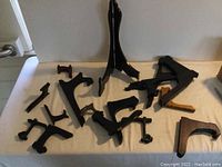 Up-close photo showing a variety of black plate stands scattered on a flat surface; all appear to be made mostly of wood and painted black; one stand is visibly damaged or broken.