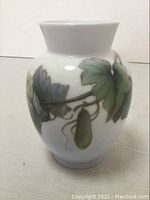 Front view of the white ceramic vase showing detailed painted vine and leaves.