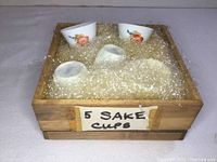 Top view of set of five sake cups snugly placed in original wooden box with packing material.