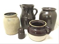 Five stoneware vessels including a brown glazed pitcher, stamped pot, brown glazed pot, insulator, and bean pot missing lid, shown together.