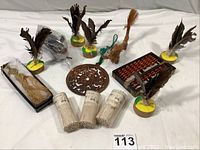 Overview of the lot showing the small wooden abacus, Balinese coin maille pig, woven dragon, several feathered Chinese kick toys, and the carved metal plaque.