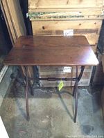 Photo showing vintage folding TV table with wooden rectangular top and visible scratches, curved wooden legs forming an X