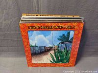 Photo of reggae vinyl record lot showing cover of "This Is Reggae Music Vol. 2" with tropical outdoor scene and foliage with fence and cloudy sky.