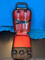 Photo showing interior of red and black bar luggage with two clear glass bottles held by leather strap