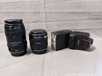 Front and side view of the Canon EF 135mm f/2.8 Soft Focus lens, Canon 35-70mm zoom lens, and Canon 420EZ flash showing all items in lot.