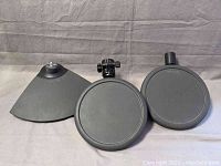 Three black Yamaha electronic drum pads on gray fabric background showing pads and mounting hardware