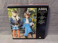 Photo of ABBA Greatest Hits vinyl album showing cover with two band members sitting on a bench in a park.