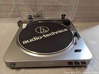 Audio Technica turntable overview with dust cover open, showing the platter with Audio Technica logo mat, tonearm, and control buttons.