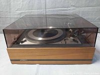 Side view of Dual 1209 turntable inside smoked dust cover showing wood base and front panel with Norsco label