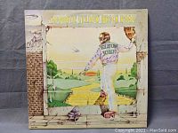 Front cover of the vinyl album showing illustrated artwork of Elton John stepping through a broken wall onto a yellow brick road, bright and detailed.