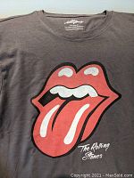 Front view of The Rolling Stones T-shirt showing the large red lips and tongue logo with text below on a charcoal grey background