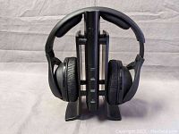 Front view of wireless headphones resting on charging base with padded ear cups and headband visible.