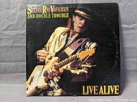 Front cover of the 'Live Alive' album showing Stevie Ray Vaughan playing guitar with a gold jacket and hat.