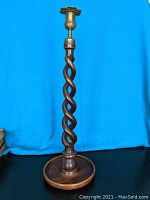 Full view of the tall barley twist candle holder showing the entire spiral column, round base, and candle cup at the top, set against a blue backdrop.