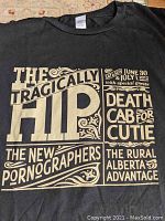 Front and back view of black XL concert T-shirt with beige print showing band names and dates.