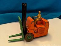 Side view of vintage orange Coventry Climax forklift with green forks and beige driver figure.