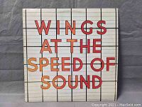 Front cover of Wings 'At The Speed Of Sound' vinyl album showing title in orange and red block letters on grid background.